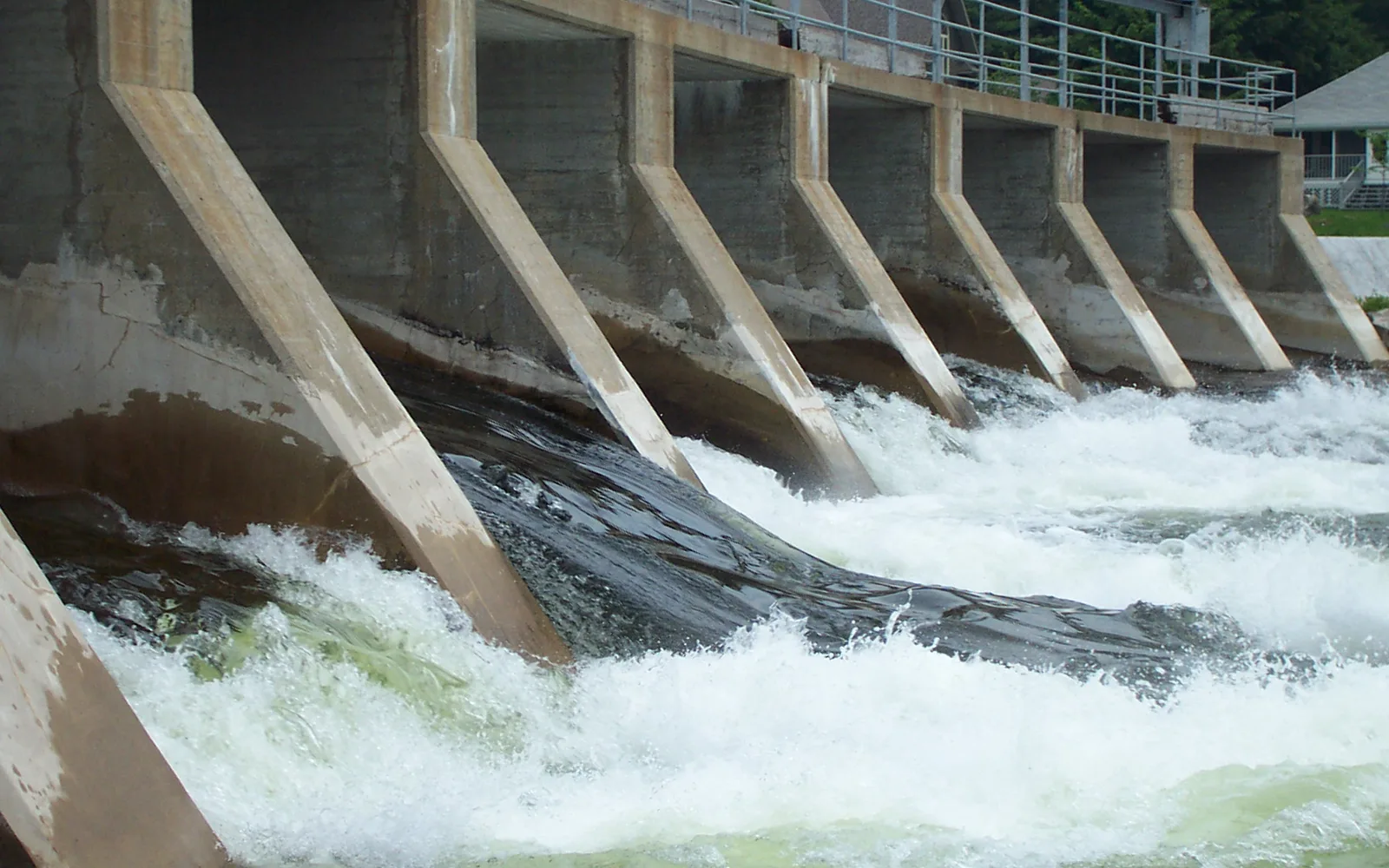 A dam holding back blue water with trees and blue sky visible across the landscape